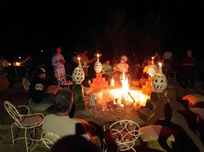 a group of people sitting around a fire at night at Luxury Desert Camp Erg Chegaga in El Gouera