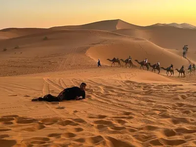a group of people riding camels in the desert at Sahara binich sercices in Merzouga