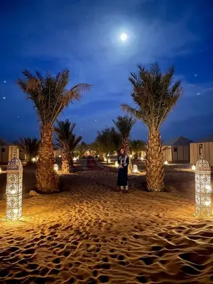 a woman standing inront of three palm trees at night at Expérience Inoubliable dans une Tente de Luxe en plein Désert de Merzouga ! in Merzouga