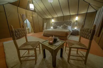 a bedroom with a bed and two chairs and a table at Camp Luxueux en plein désert de Merzouga in Merzouga