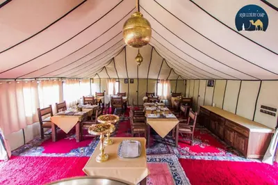 a dining room with tables and chairs in a tent at Camp Luxueux en plein désert de Merzouga in Merzouga