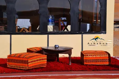a table and three ottomans on a red rug at Sahara Luxury Camp - Nuit de rêve dans le désert de Merzouga ! in Merzouga
