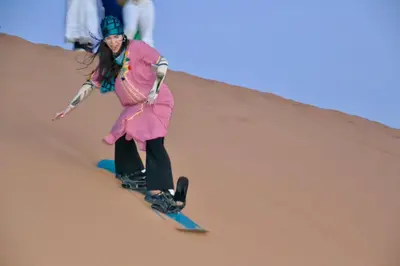 a woman riding a snowboard down a sand dune at Sahara Luxury Camp - Nuit de rêve dans le désert de Merzouga ! in Merzouga