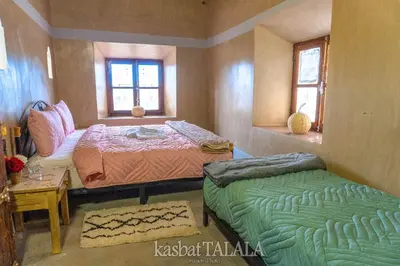 a bedroom with two beds and a table and two windows at Kasbah Talala in Skoura