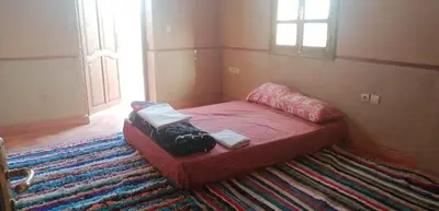 a small bedroom with a red bed on a rug at DAR AGLMOUZ -Ighir aghzzaf- in Kalaat MGouna