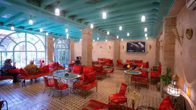 a room with red chairs and tables and a tv at Riad Golden Mansour in Meknès