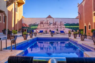 a swimming pool with chairs and a mural on a building at lmtounipalace in Ouarzazate
