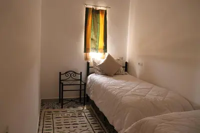 a bedroom with two beds and a window and a table at Dar margoum in Marrakech