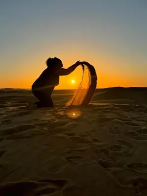 a woman in the sand with a surfboard in the sunset at Sahara Magic Luxury Camp & Camel trek in Merzouga