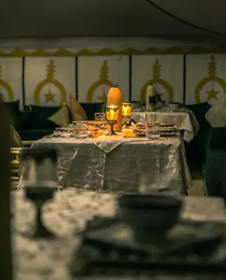 a table with plates of food and a lamp on it at Merzouga Luxurious Camp in Merzouga