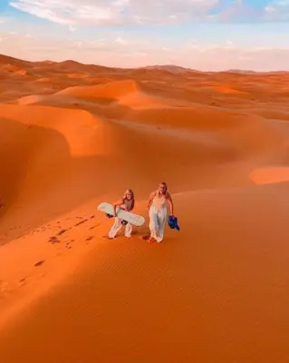 two women standing in the desert with their surfboards at White Camp Desert Safari in Merzouga