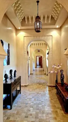 a hallway of a building with a table and a chandelier at Villa Alcázar Marrakech in Had Abdallah Rhiat