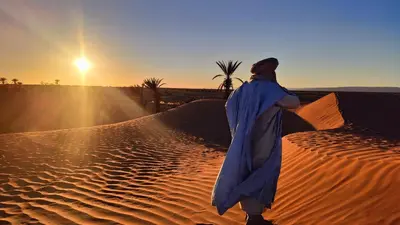 a woman walking through the desert at sunset at Nomads Heaven Camp in Mhamid