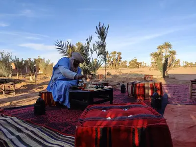 a woman sitting on a rug in the desert at Nomads Heaven Camp in Mhamid