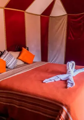 a bedroom with a bed with red sheets and orange pillows at Sahara mirage camp in Merzouga