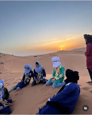 a group of people sitting in the desert at sunset at Mars Desert Camp Merzouga in Merzouga