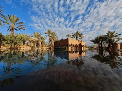 a reflection of a mosque in the water with palm trees at Lodge Hara Oasis in Agdz