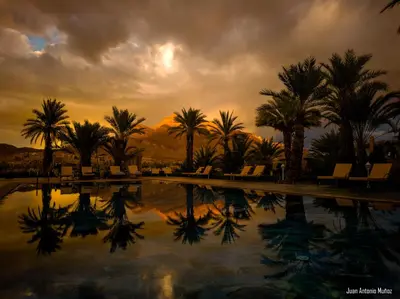a pool with palm trees and a cloudy sky at Lodge Hara Oasis in Agdz