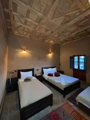 a bedroom with two beds and a wooden ceiling at Kasbah Ennakb in Nkob
