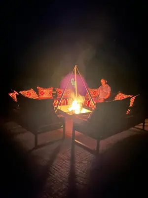 a man sitting in front of a fire at night at Andromeda Desert Astro Camp in Derkaoua