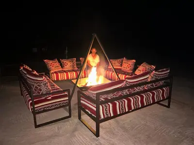 a man standing in front of a fire with two chairs at Andromeda Desert Astro Camp in Derkaoua
