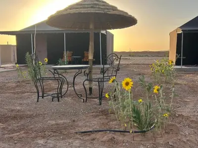 a table and chairs with an umbrella and flowers at Andromeda Desert Astro Camp in Derkaoua