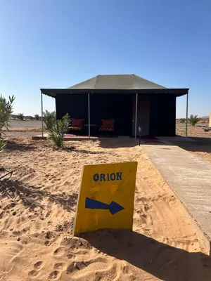aiction sign in the sand in front of a building at Andromeda Desert Astro Camp in Derkaoua