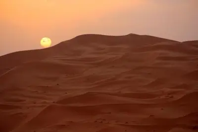 an image of the sun rising over a desert at merzouga desert camp in Merzouga