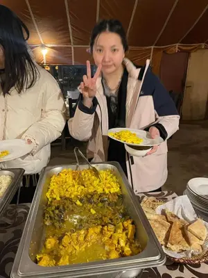 a woman holding a plate of food and making a peace sign at Desert Nights Camp in Merzouga