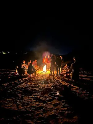 a group of people standing around a fire on a beach at night at Desert Nights Camp in Merzouga