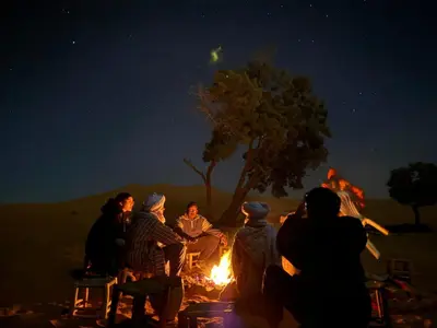 a group of people sitting around a fire at night at Desert Nights Camp in Merzouga