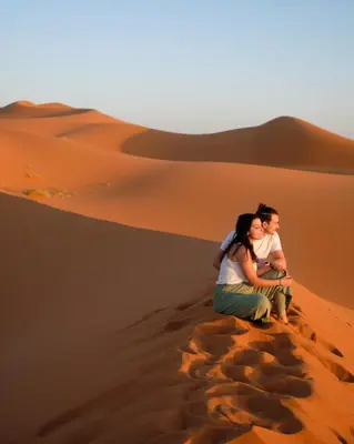 a couple sitting on a sand dune in the desert at Sahara Desert Camp in Merzouga