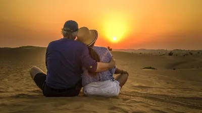 a man and woman sitting in the desert watching the sunset at Sahara Desert Camp in Merzouga