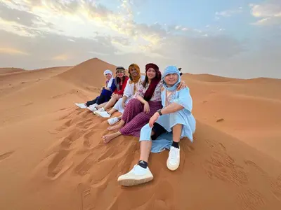 a group of women sitting on the sand in the desert at Sahara Desert Camp in Merzouga