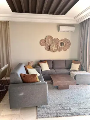 a living room with a couch and a table at Appartement Cosy avec grande terrasse et piscine en face du stade Can2025 in Dar Rahal Ben Saïd