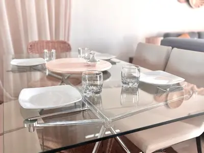 a glass table with chairs and glasses on it at Appartement Cosy avec grande terrasse et piscine en face du stade Can2025 in Dar Rahal Ben Saïd