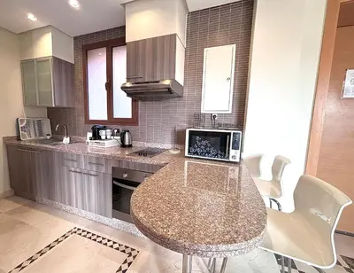 a kitchen with a table with a laptop on it at Appartement Cosy avec grande terrasse et piscine en face du stade Can2025 in Dar Rahal Ben Saïd