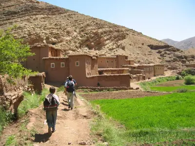 two people walking down a dirt road near a village at Auberge Sremt in Sremt