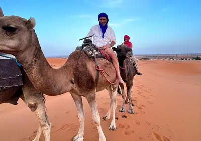 two people riding on the back of a camel in the desert at Merzouga nights camp& excursions in Merzouga