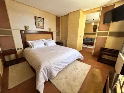 a bedroom with a white bed and a living room at Hotel Bab Mansour in Meknès