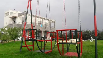 a swing set in a park with a building in the background at la ferme zine in Ain Cheggag