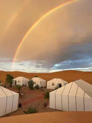 a rainbow over a group of tents in the desert at Safari trips Morocco luxury camp in Merzouga