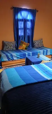 two beds in a room with a blue curtain at Moha House in Merzouga