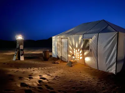 a tent in the sand with a lighthouse in the background at Camp Sahara Feeling in El Gouera