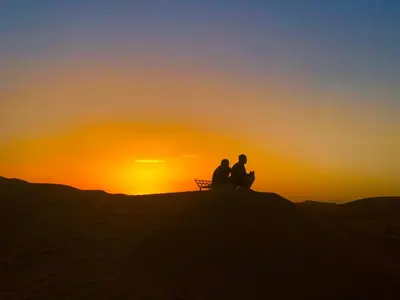 two people sitting on a bench watching the sunset at Pueblo Touareg - Private Tents in Merzouga