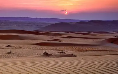 a desert with a sunset in the background at Erg chagaga in Mhamid