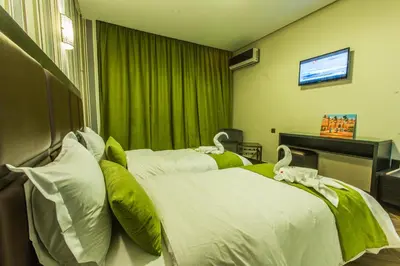two beds in a hotel room with green curtains at Hotel Swani in Meknès