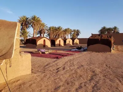 a group of buildings in the desert with palm trees at Hammadi Camp in Mhamid