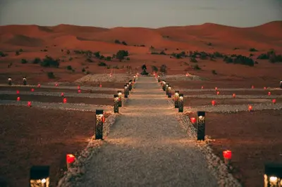 a pathway in the middle of a desert with red candles at Antares Desert Camp in Merzouga