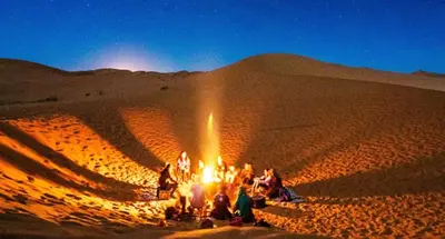 a group of people sitting around a fire in the desert at Fabulos Merzouga Luxury Camp in Hassilabied